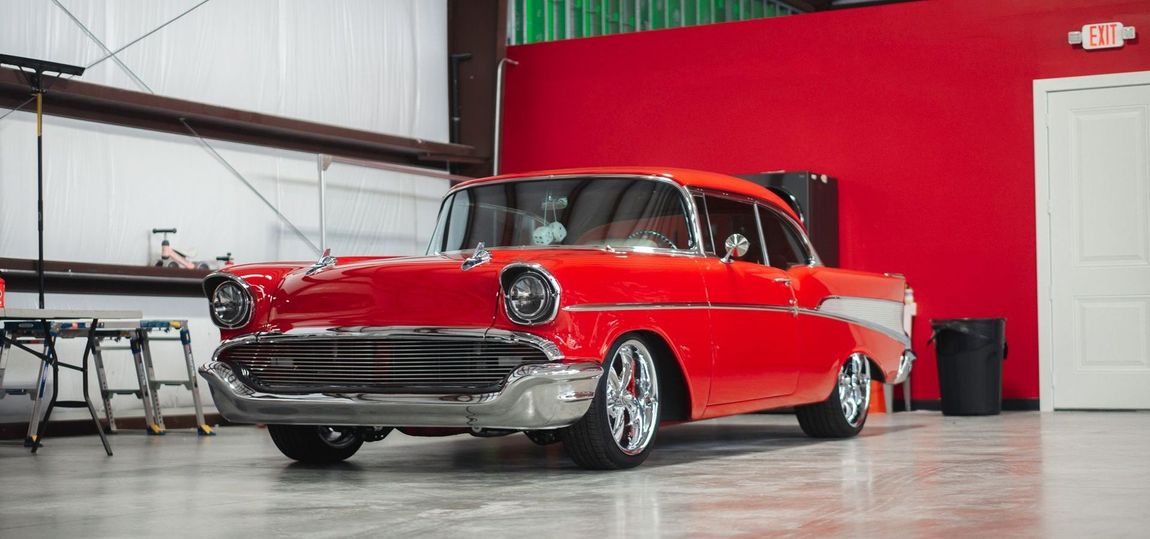 Red classic car displayed in a showroom with a red wall and polished concrete floor.