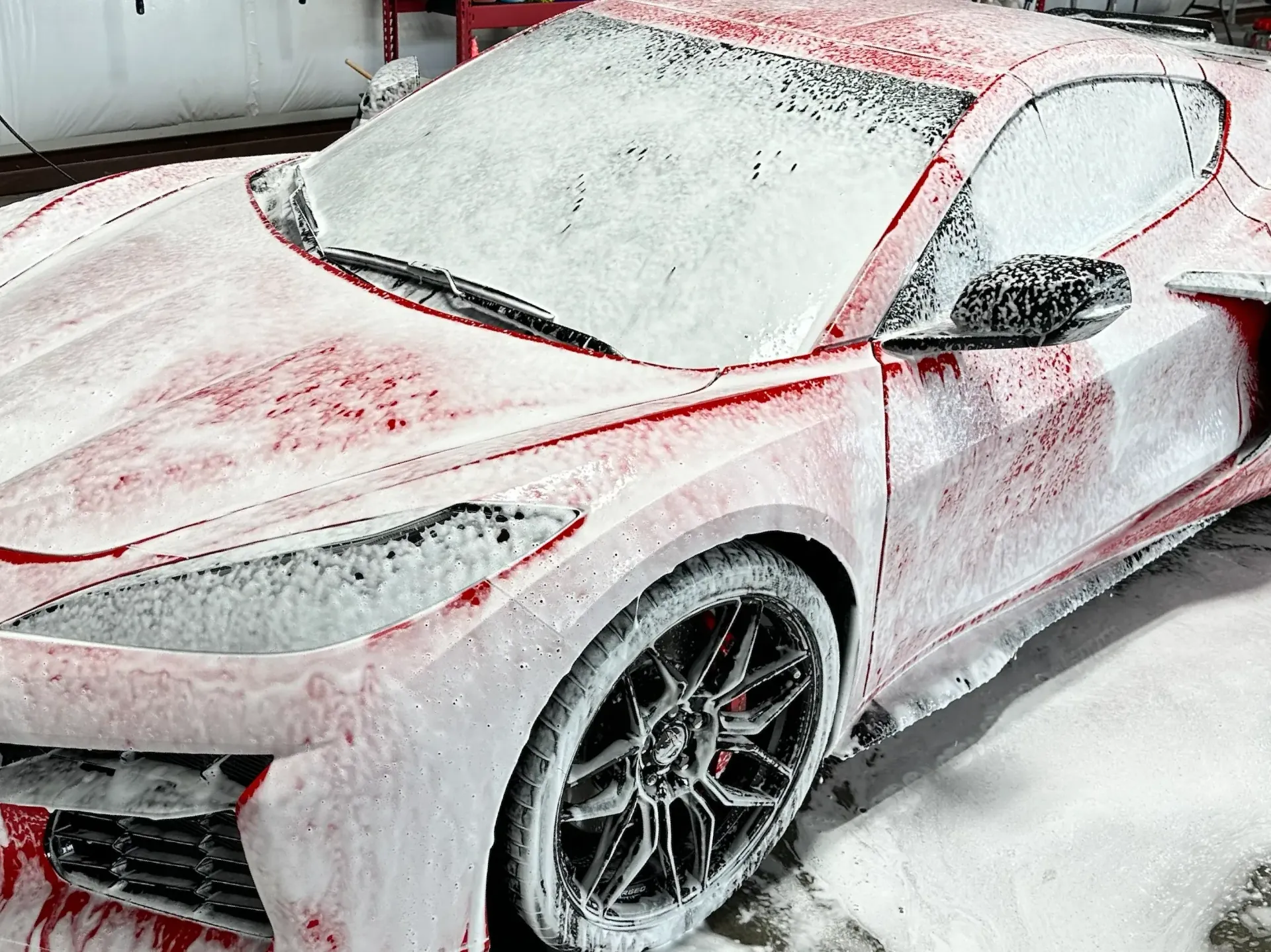 Red sports car covered in snow in a driveway or garage area.