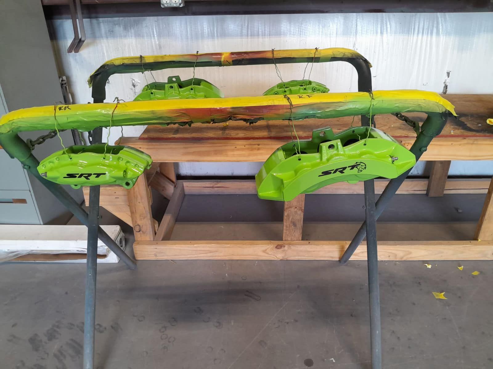 Green clamping saw horses holding a long wooden plank in a workshop.