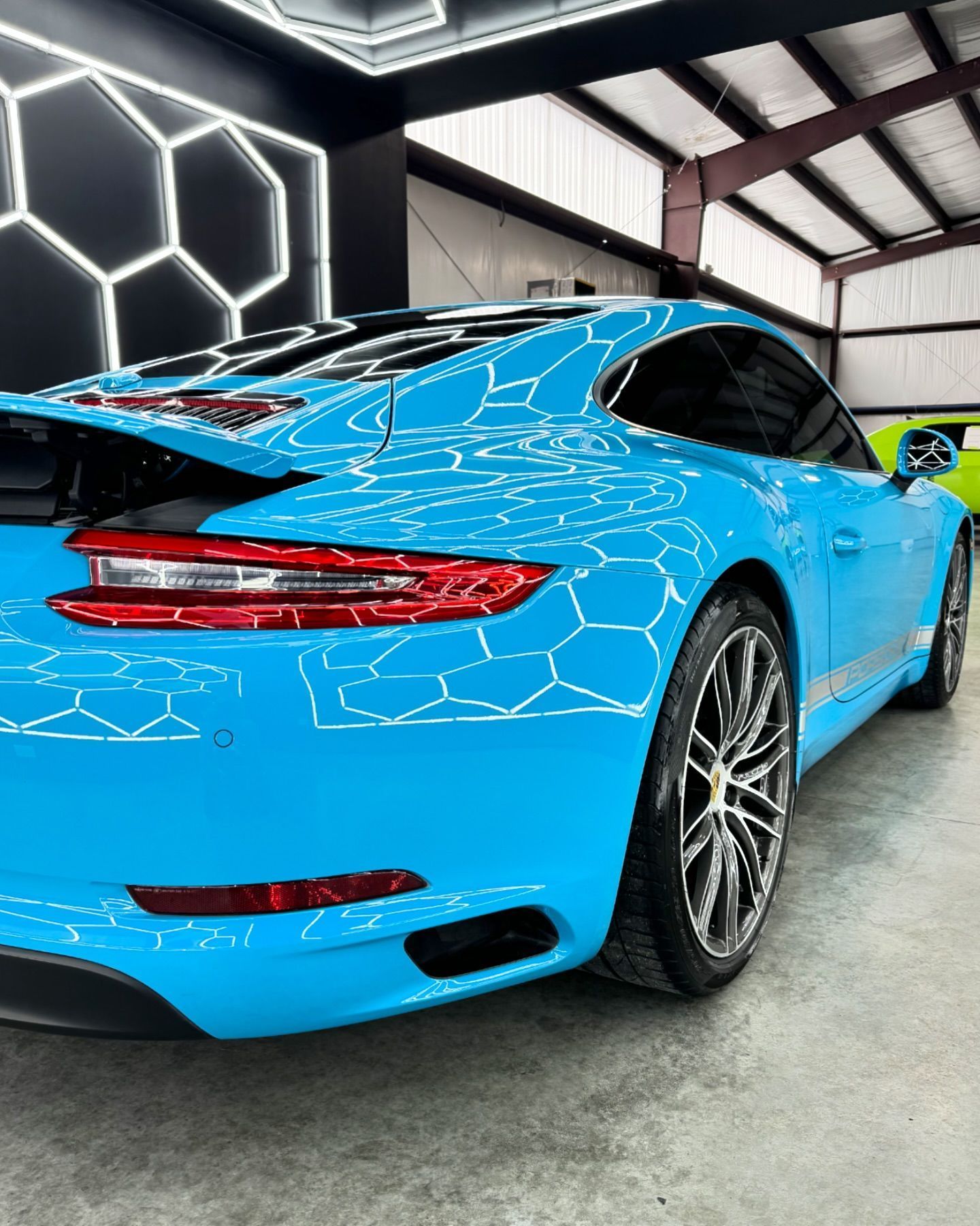 Bright blue sports car in a garage, viewed from the rear with hexagon light reflections on its body.