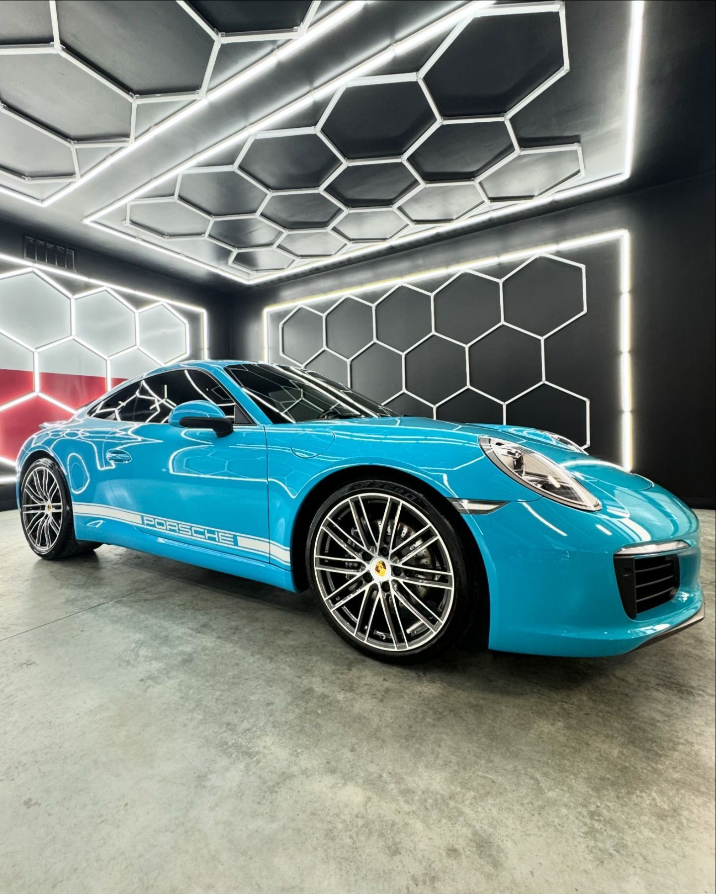 Bright blue sports car parked indoors against a glowing hexagonal wall.