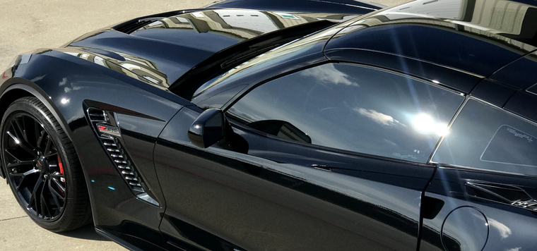 Black sports car with sleek body and tinted windows, viewed from above in sunlight