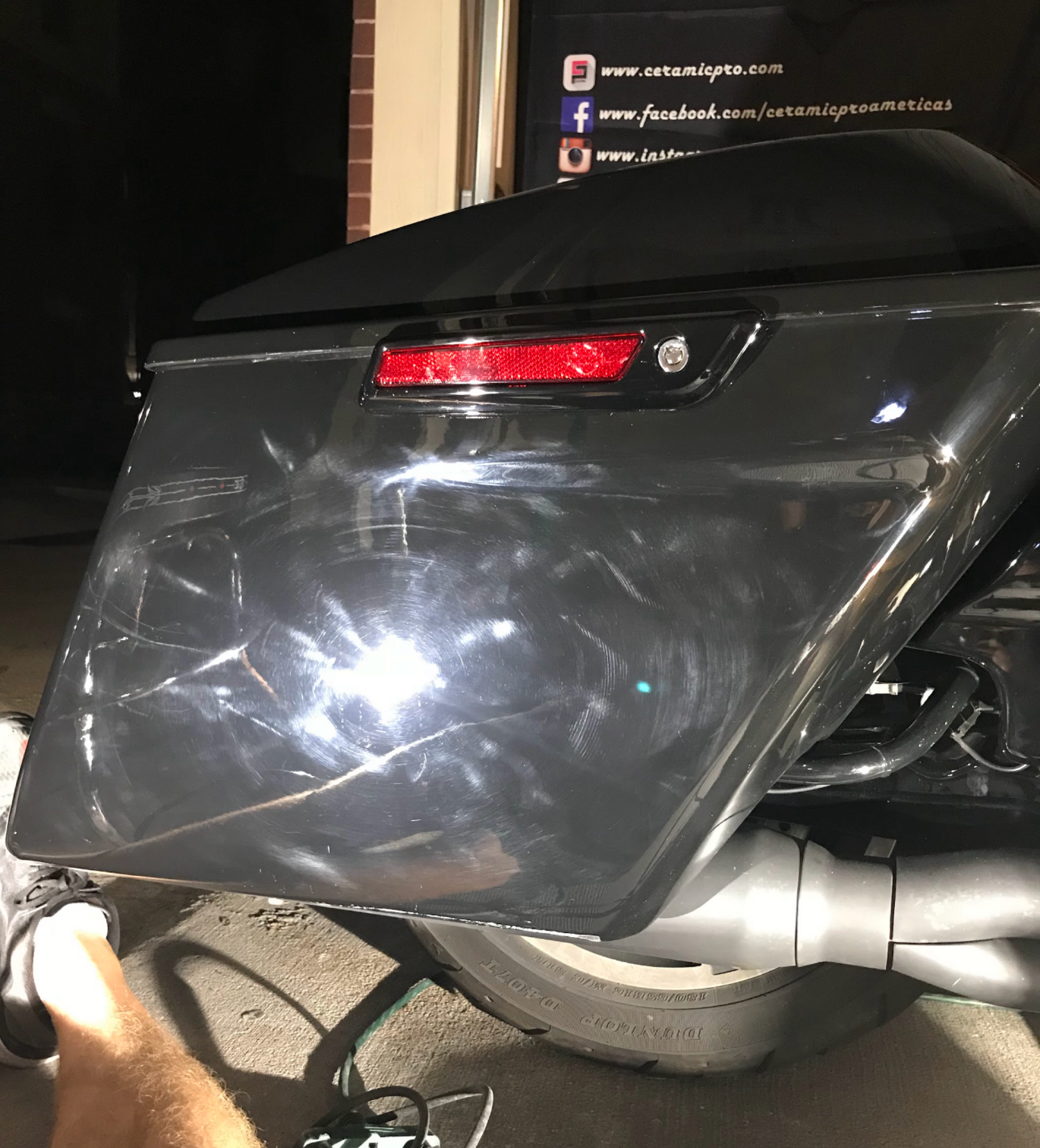 Close-up of a black motorcycle side bag with a red reflector and visible exhaust pipe.