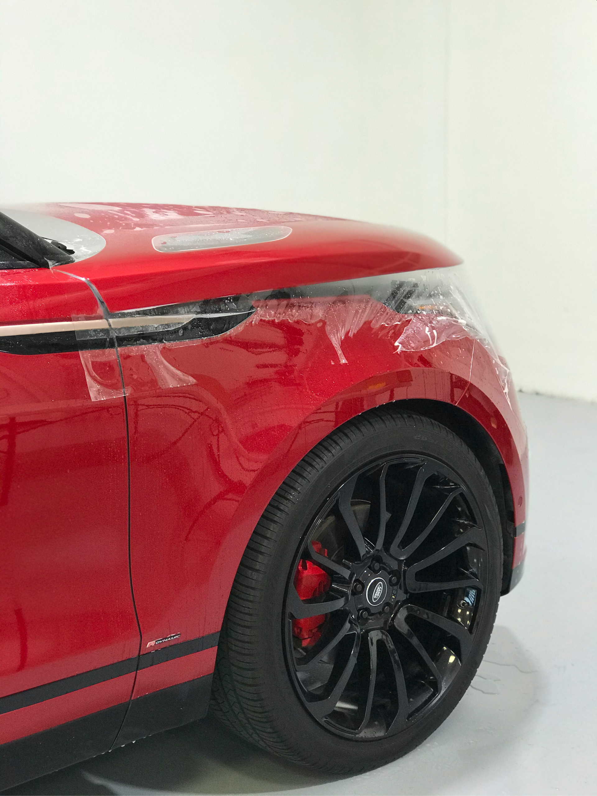 Close-up of a red car’s front side with black wheel in a white studio.