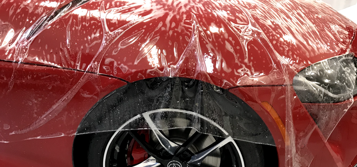 Red car partially covered in clear plastic, showing front wheel and headlight