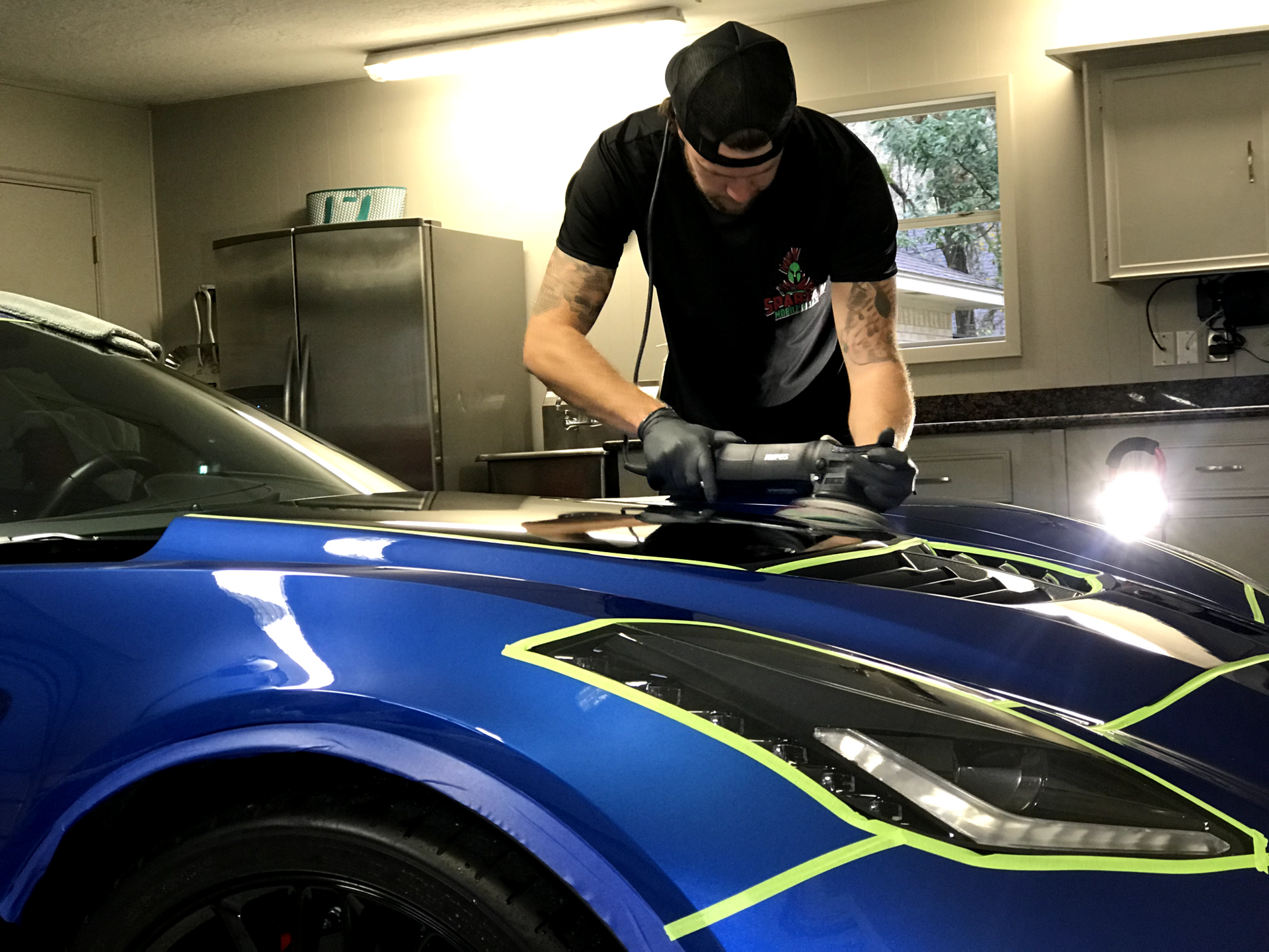Person polishing a blue sports car hood in a garage