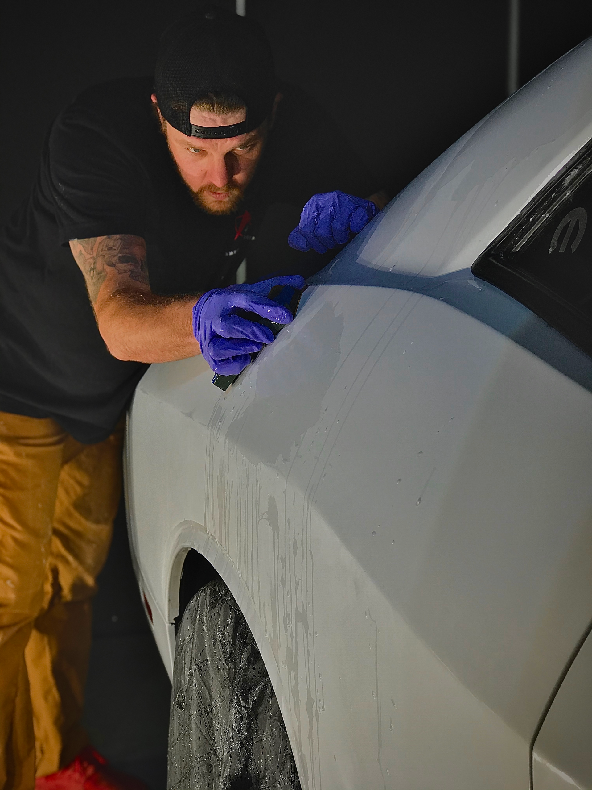 Person polishing a white car in a garage with purple gloves