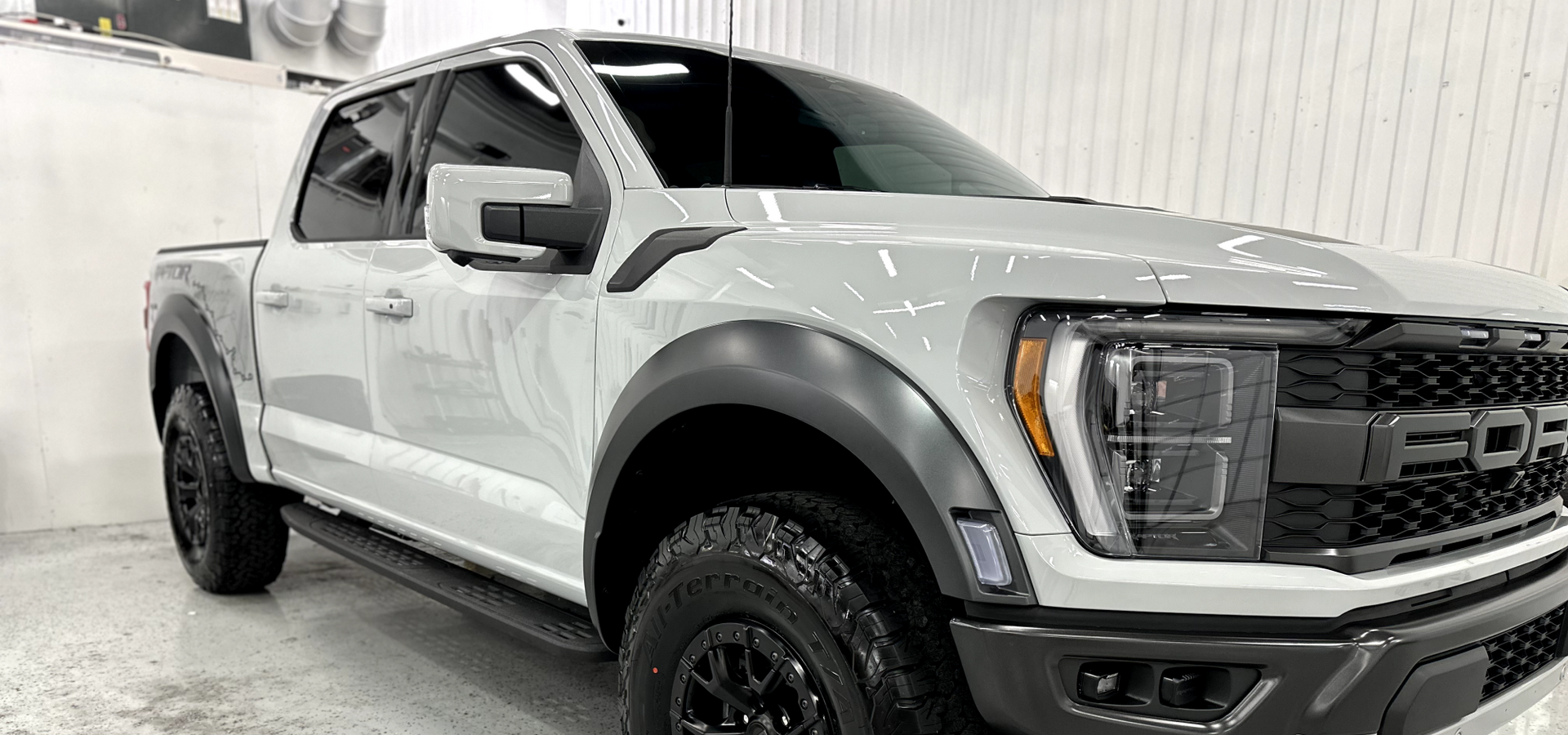 White Ford pickup truck in a studio, shown front-left with black trim and off-road tires