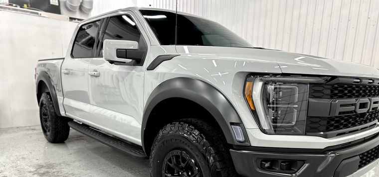 White Ford pickup truck in a showroom, front-left view with black trim and off-road tires