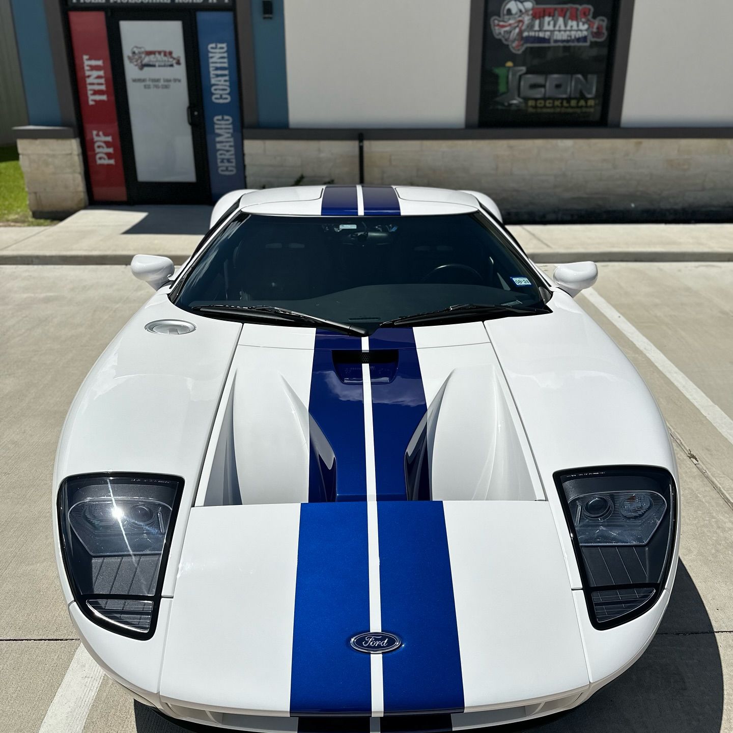 White sports car with blue racing stripes parked outside a storefront