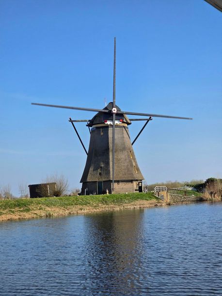 Traditional windmill by a calm blue river under a clear sky.