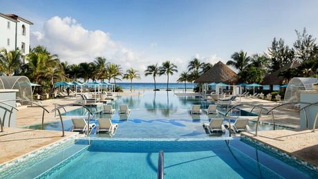 Luxury resort pool with blue water, lounge chairs, umbrellas, and palm trees overlooking the ocean.
