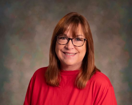 Smiling person in a red top with glasses against a softly blurred studio background