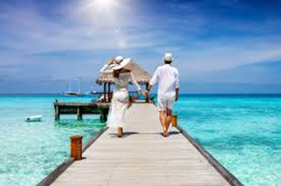 Couple walking on a wooden pier toward turquoise ocean under a bright blue sky