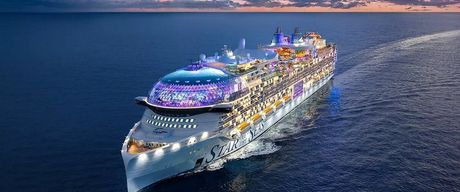 Large cruise ship lit with colorful lights sailing on open water at dusk