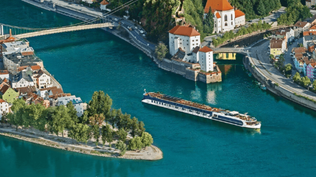 Aerial view of a turquoise river with a long boat, bridges, and colorful riverside buildings