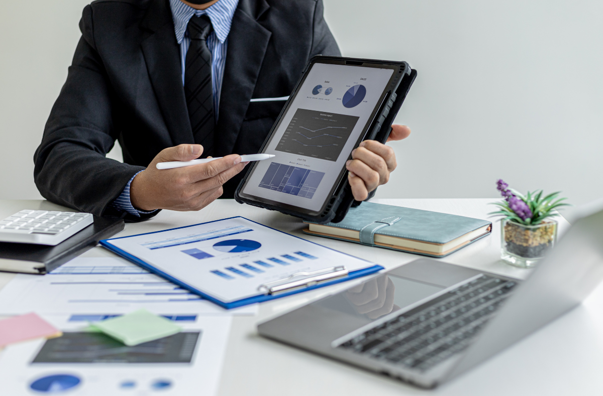 A man is sitting at a desk holding a tablet and pointing at it.