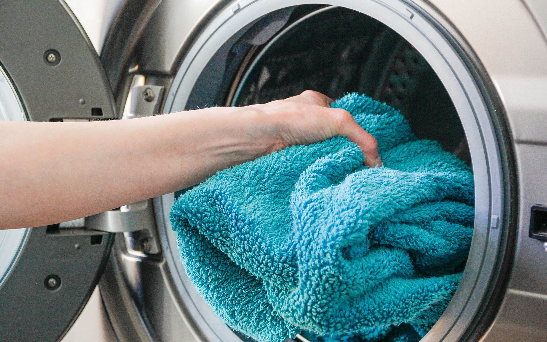 A person is putting a blue towel in a washing machine.