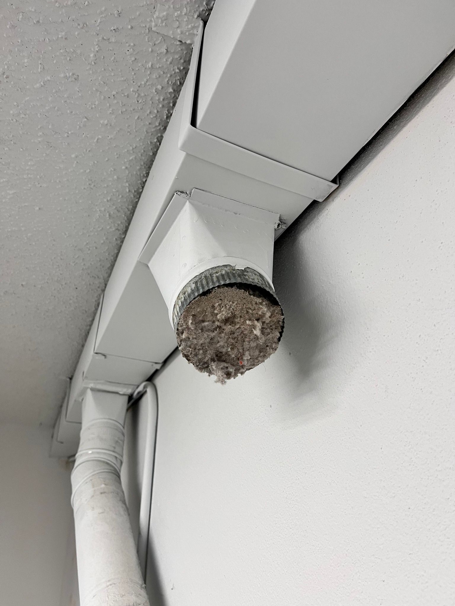 A bird nest is sitting on top of a white pipe on a wall.
