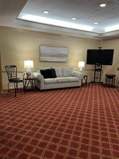 Hotel-style lounge with beige sofa, lamps, TV, and red patterned carpet