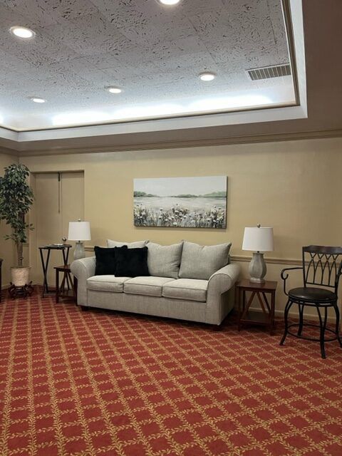 Empty hotel lobby seating area with beige sofa, lamps, chairs, and red patterned carpet