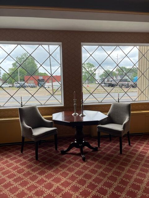 Two chairs and a round table by large windows in a carpeted room