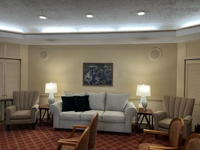 Living room with white sofa, lamps, armchairs, and a framed painting on the wall.