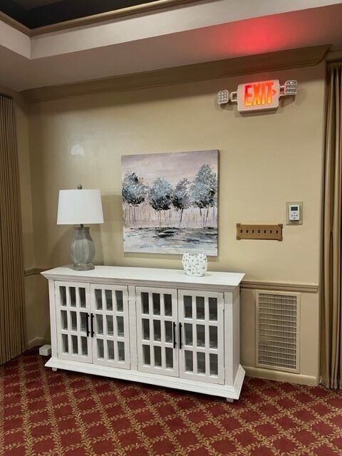 White cabinet with lamp and artwork in a beige hallway with red carpet and EXIT sign