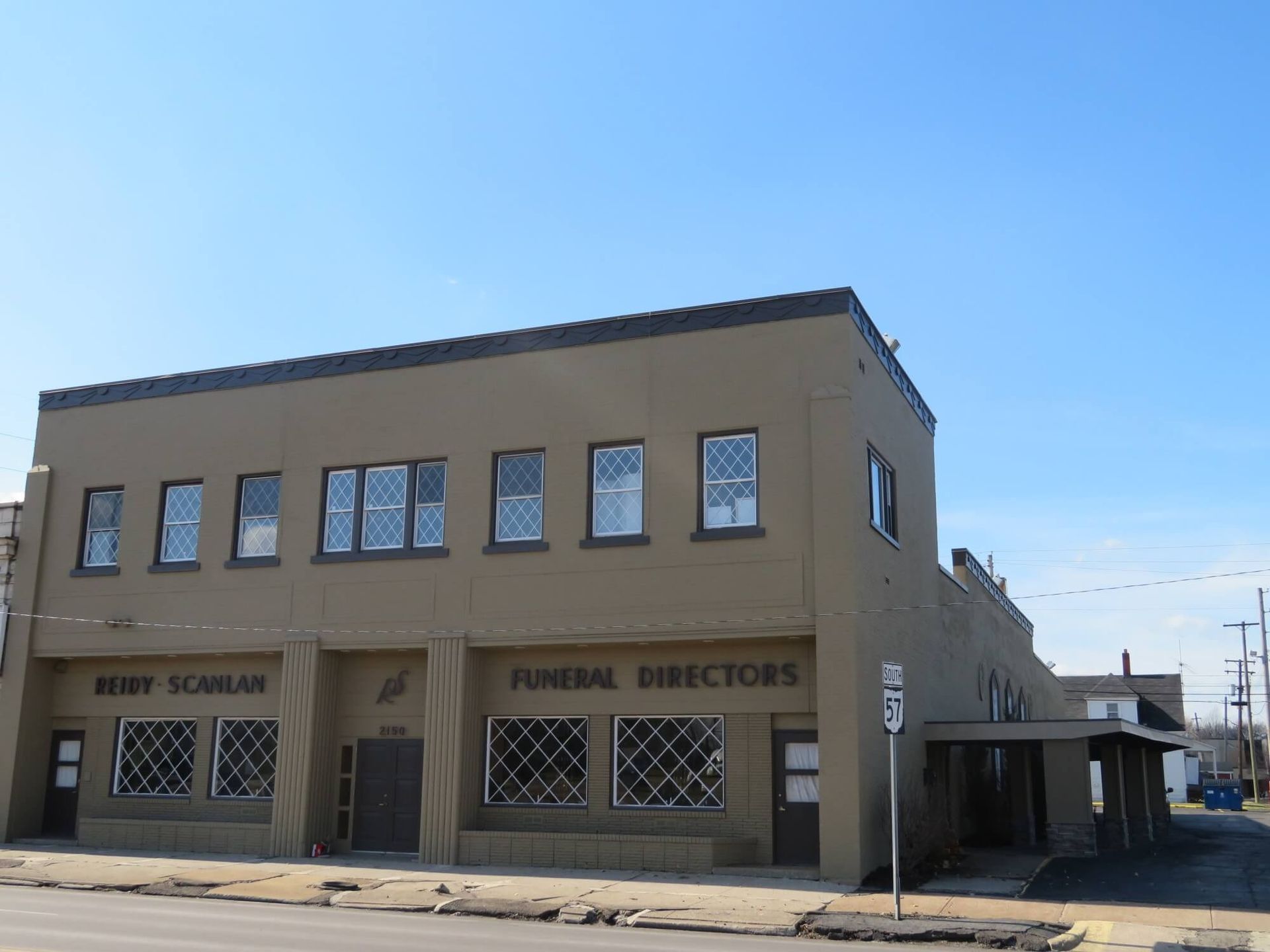 Street corner funeral home with tan stucco facade and blue sky.