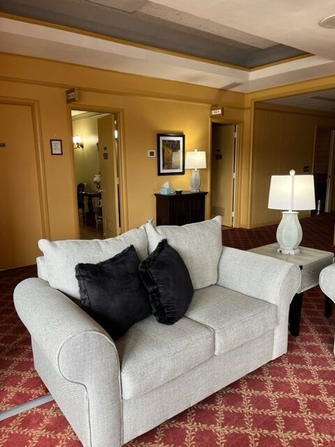 Plush white sofa with black pillows in a warm-toned hotel lounge, beside a side table and lamp.