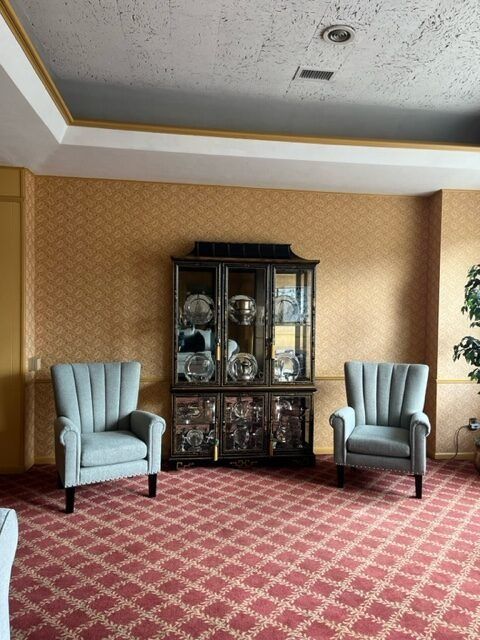 Living room with patterned carpet, two light blue armchairs, and a dark wooden china cabinet.