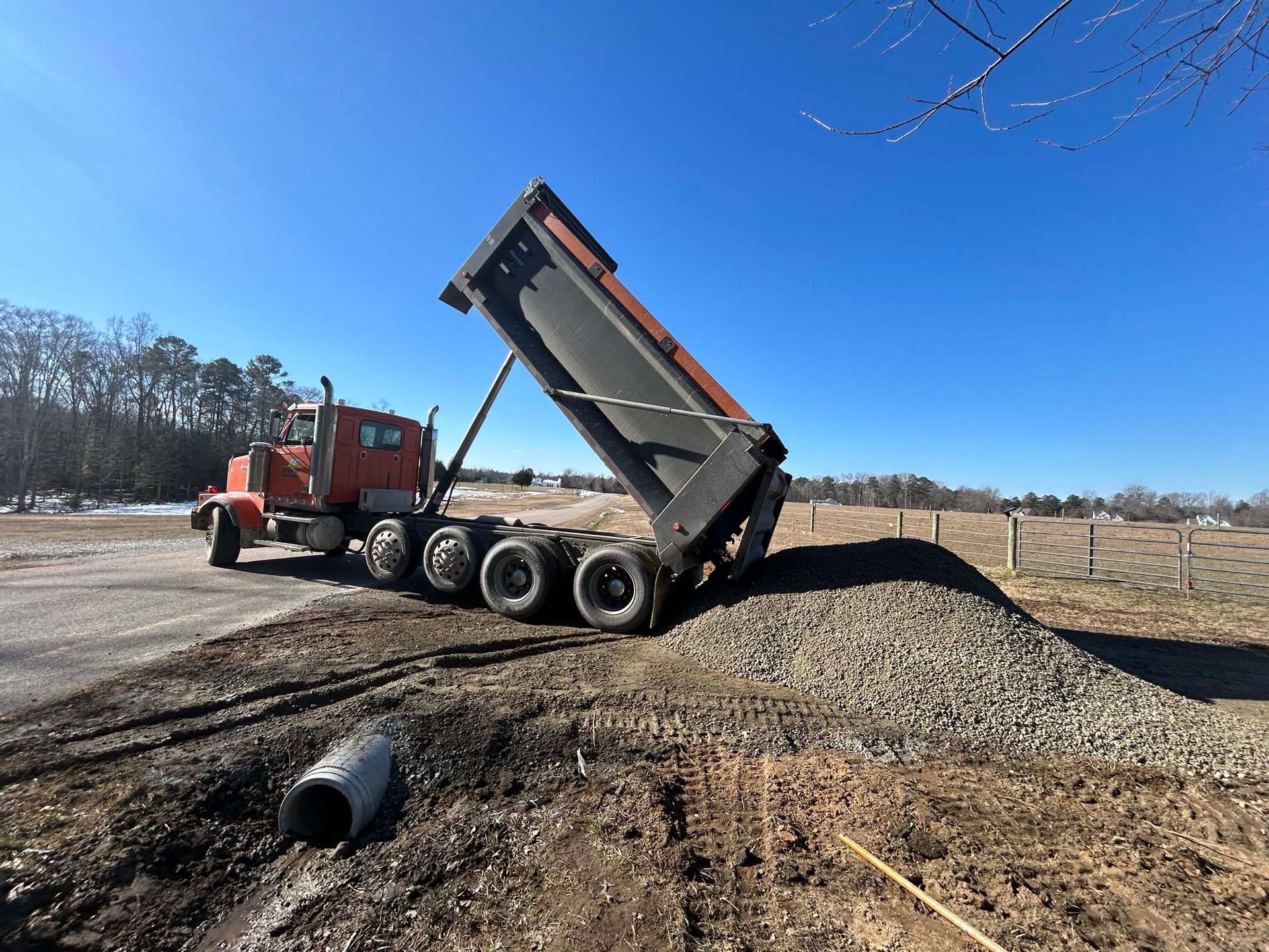 Red dump truck tipping gravel from raised bed at a construction site under a clear blue sky