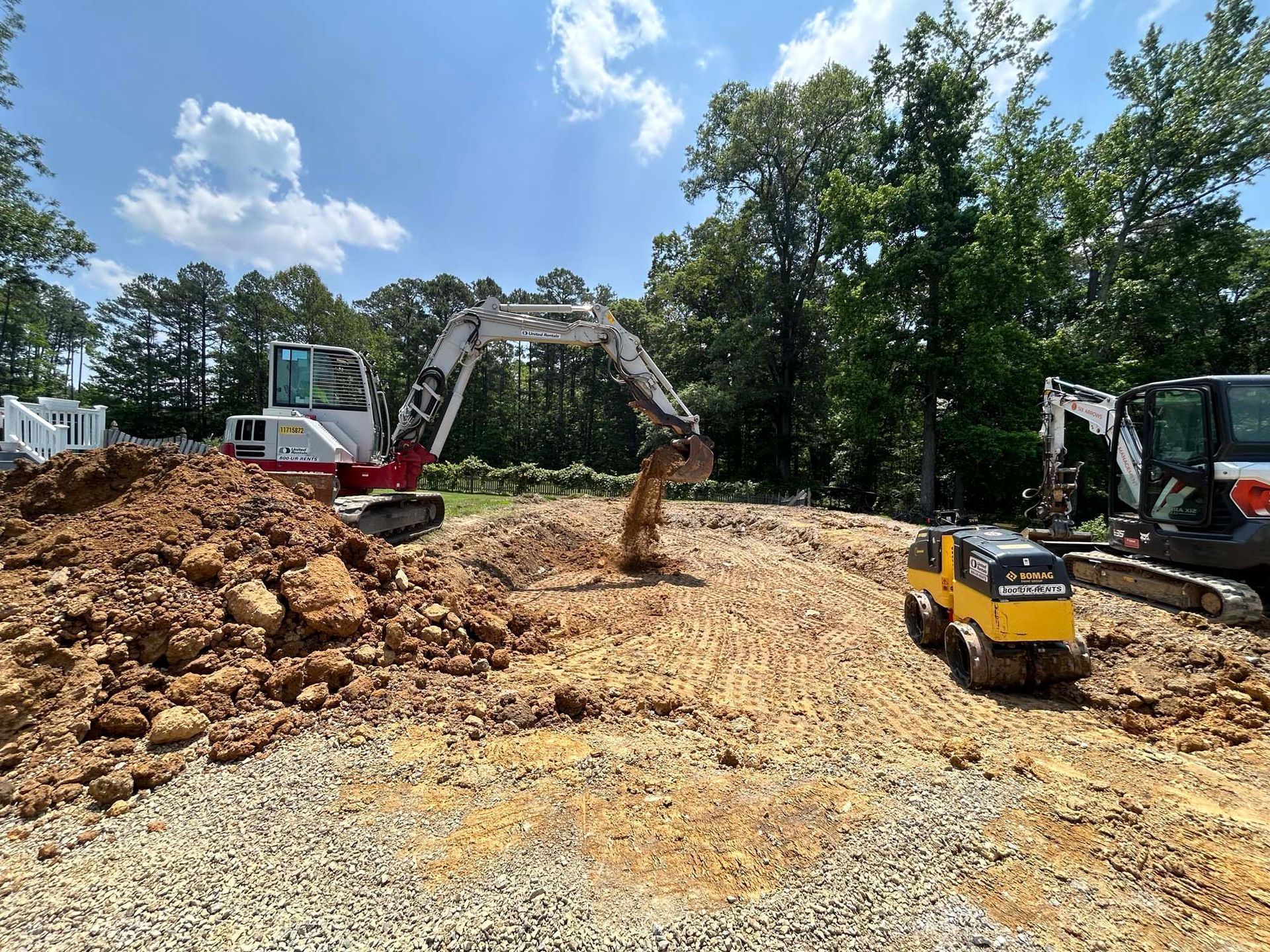 Construction site with excavator, bulldozer, and dirt piles under a partly cloudy sky
