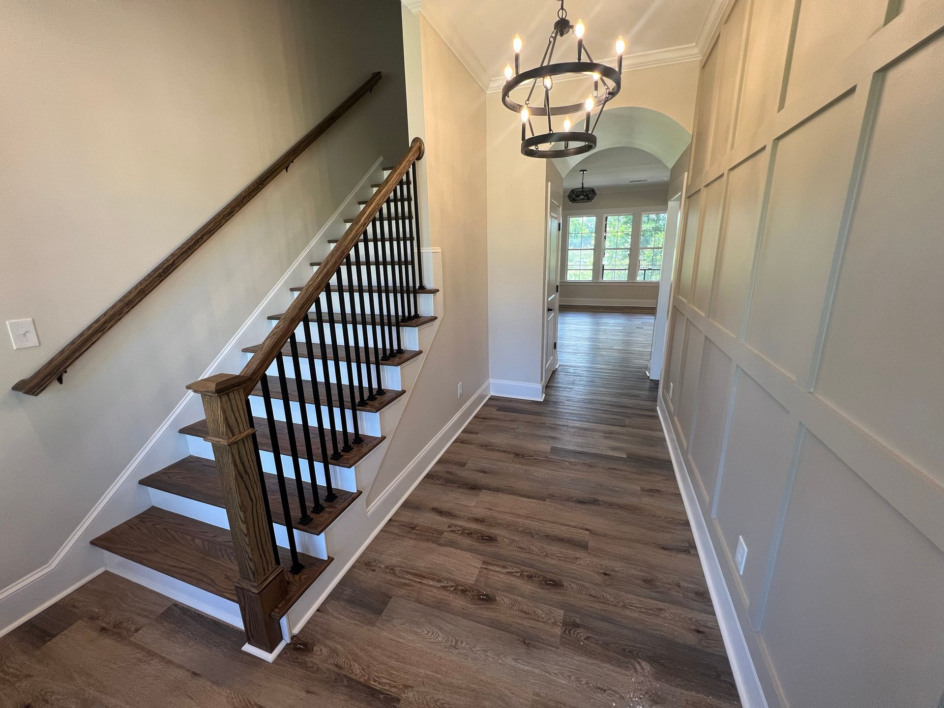 Entryway with staircase and hardwood flooring, chandelier, and paneled wall.