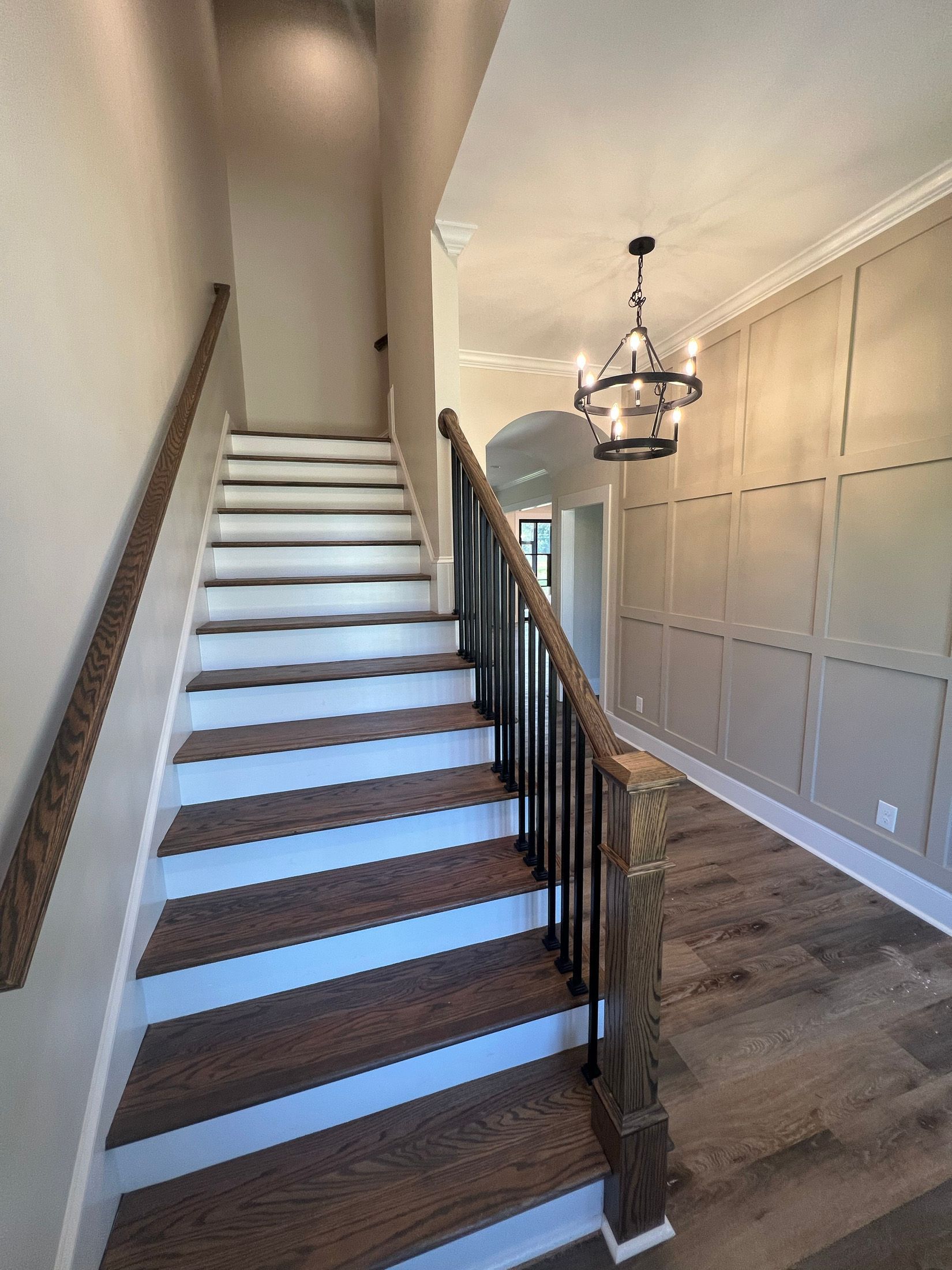 Staircase with wooden steps, a black railing, and a decorative chandelier. The walls are light beige with a wood-paneled wall.
