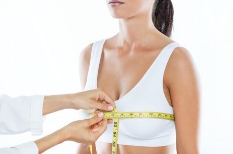 Measuring a woman's bust with a tape measure during a fitting, showing a white bra