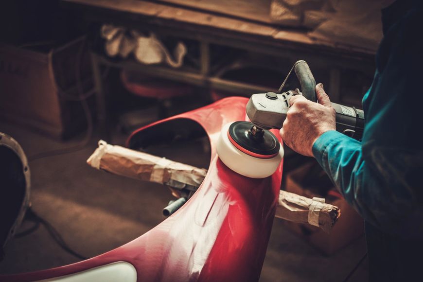 Persona che utilizza un elettroutensile per lucidare il parafango rosso di un'auto in un'officina.