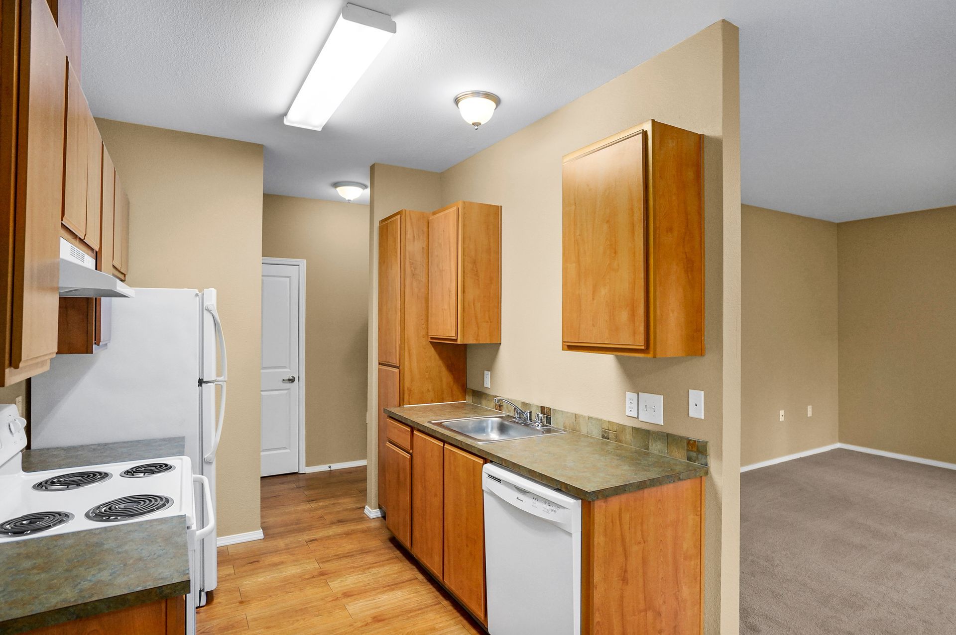 A kitchen featuring wooden cabinets, a white refrigerator, a dishwasher, a stainless steel sink, and light wood flooring.