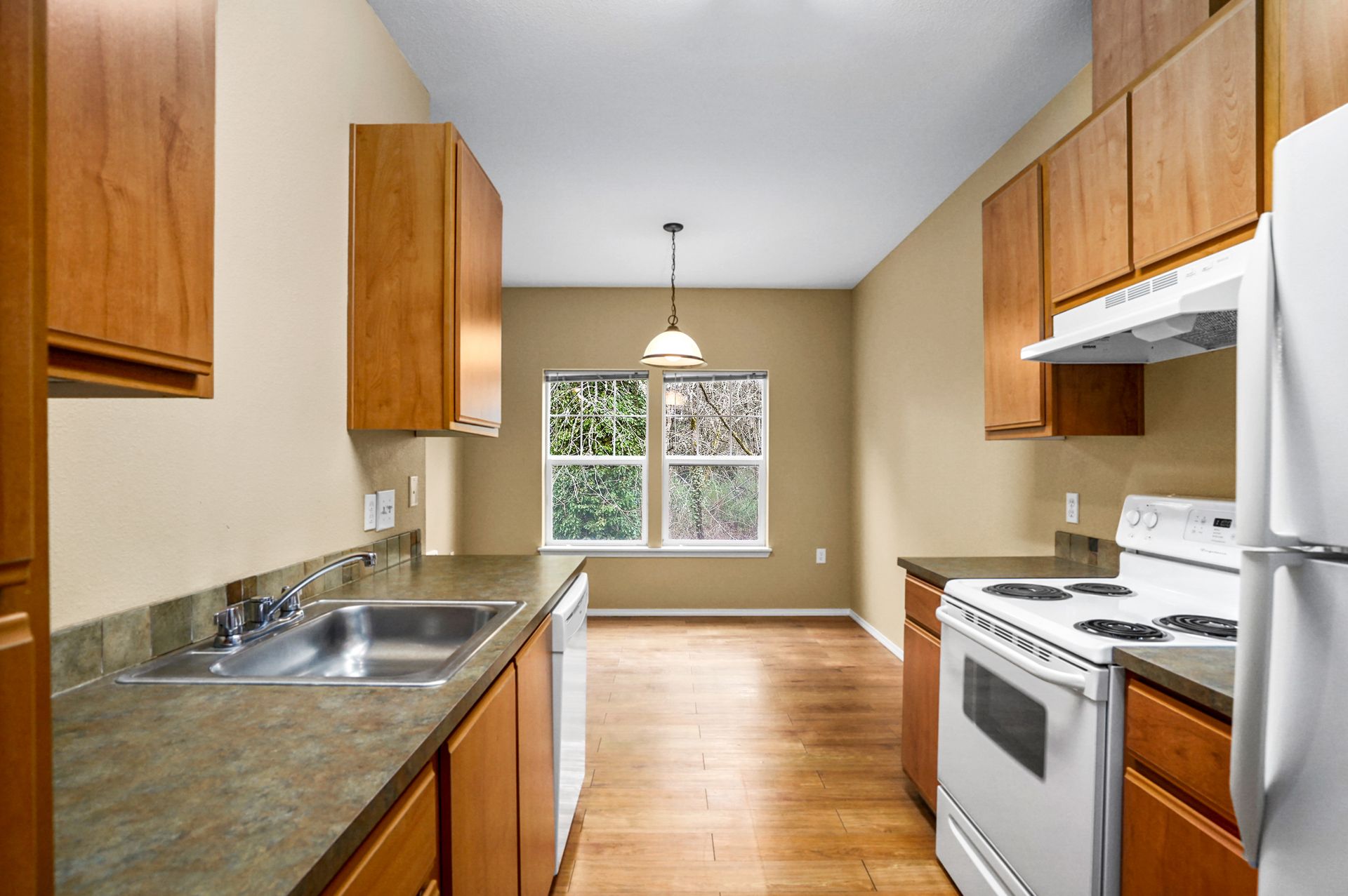 Galley kitchen with wood cabinets, laminate counters, white stove and fridge, stainless sink, and windowed dining nook.