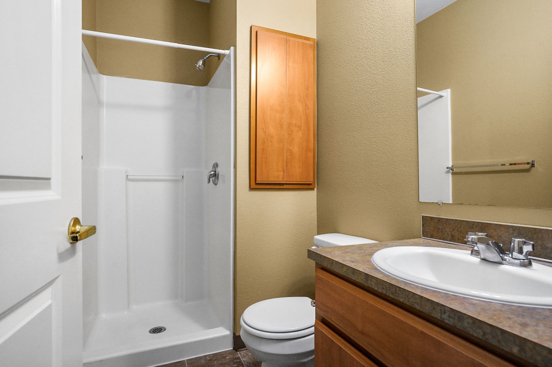 Bathroom with white shower stall, toilet, wood vanity, laminate countertop, sink, mirrored cabinet, and beige walls.