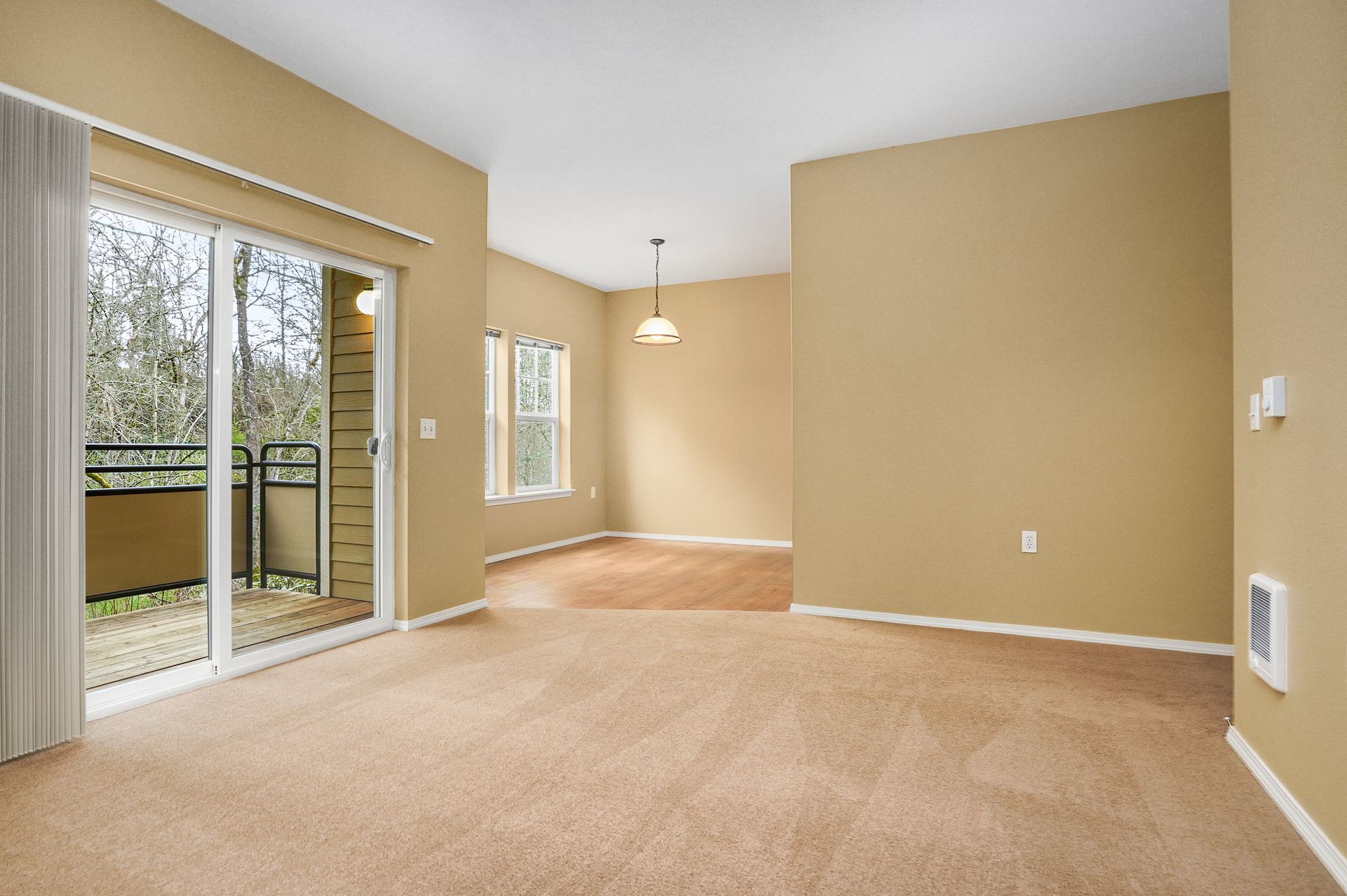 Spacious living and dining area with beige walls, carpeted floors, sliding glass door to a balcony, and windowed dining nook.