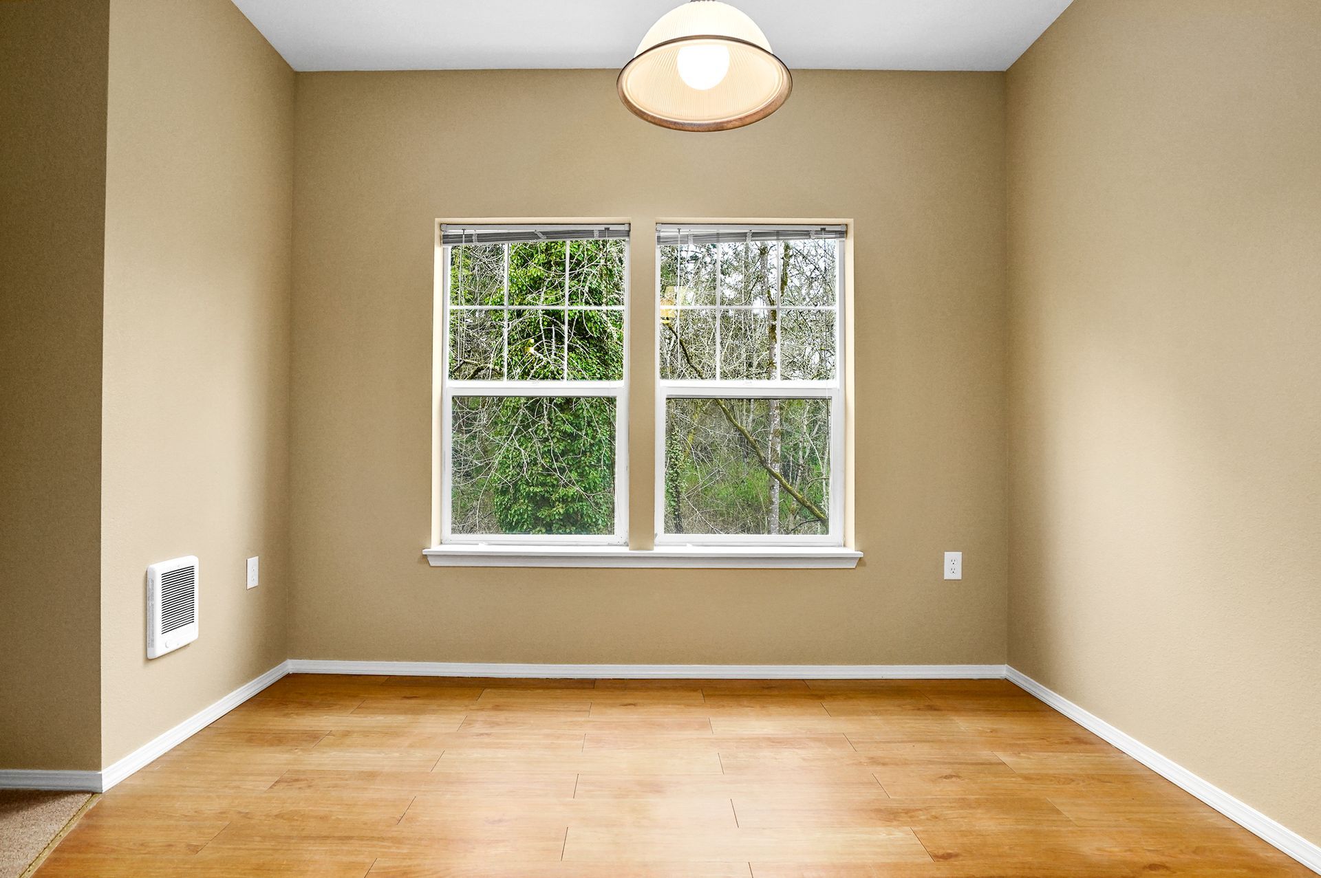 Dining area with wood flooring, beige walls, two large windows, and a pendant light, bringing in natural light.