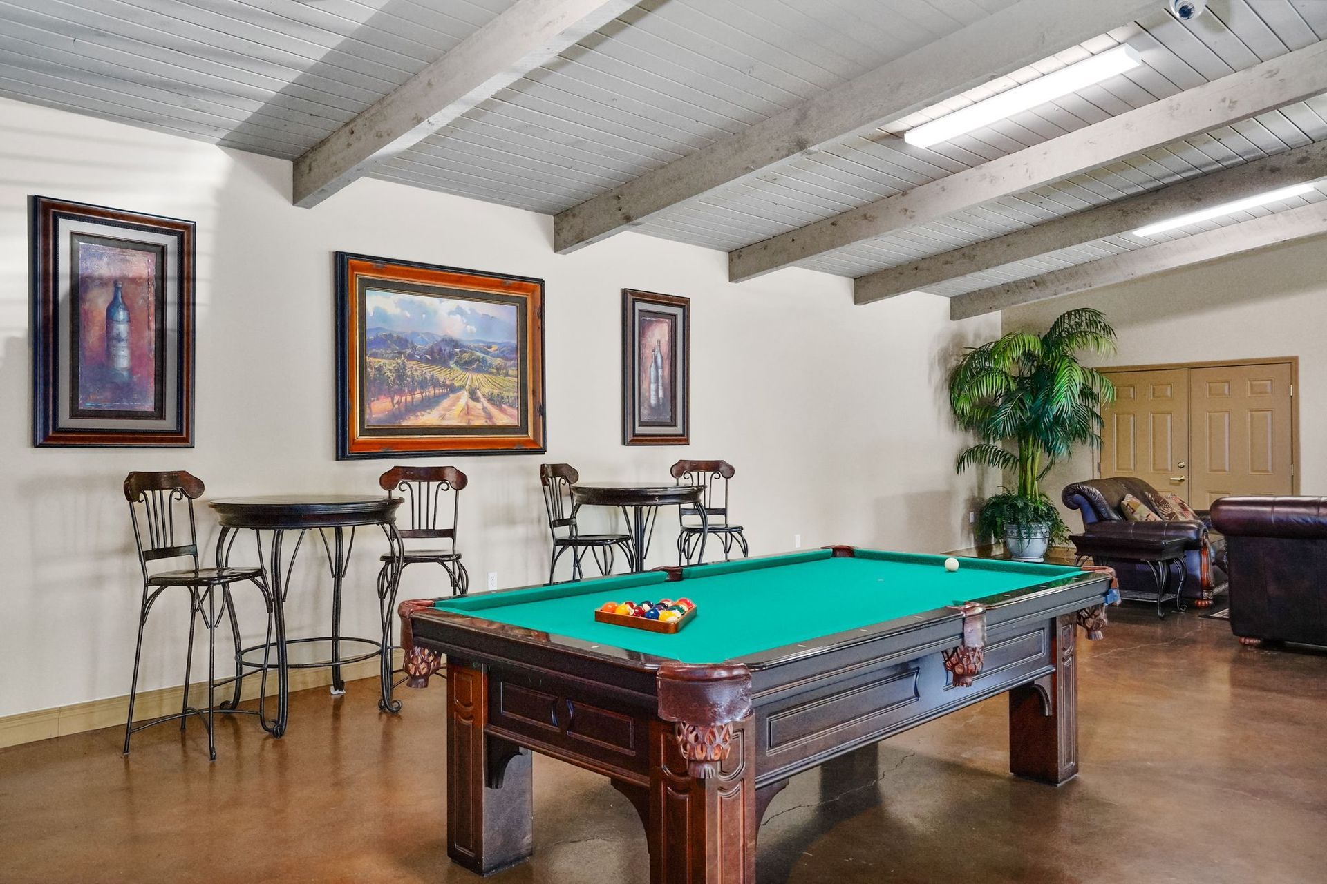 Game room with a pool table, bar-height tables and stools, framed wall art, polished floors, and exposed ceiling beams.