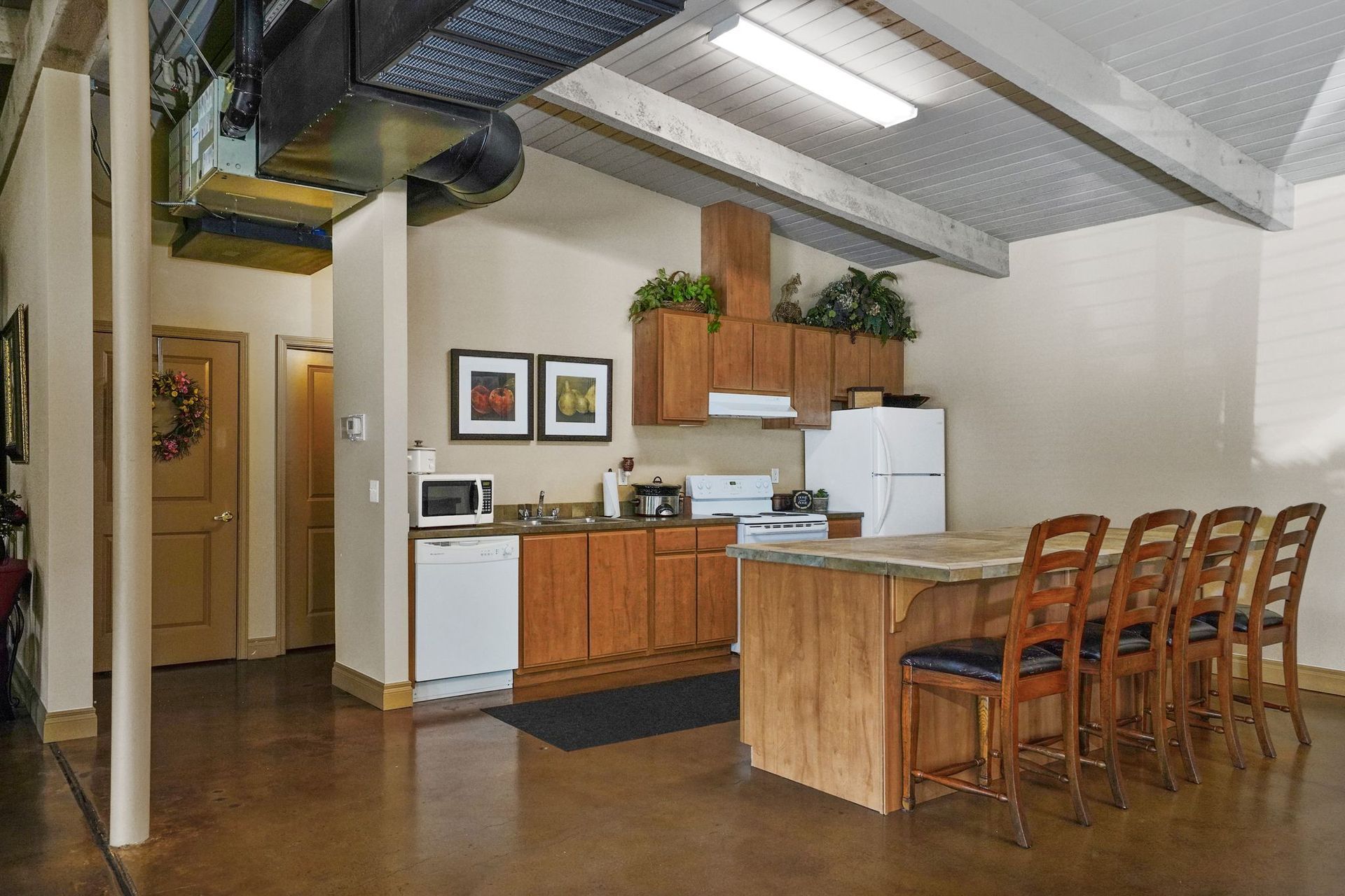 Open galley kitchen with wood cabinets, laminate counters, white appliances, wood floors, and adjacent carpeted living area.