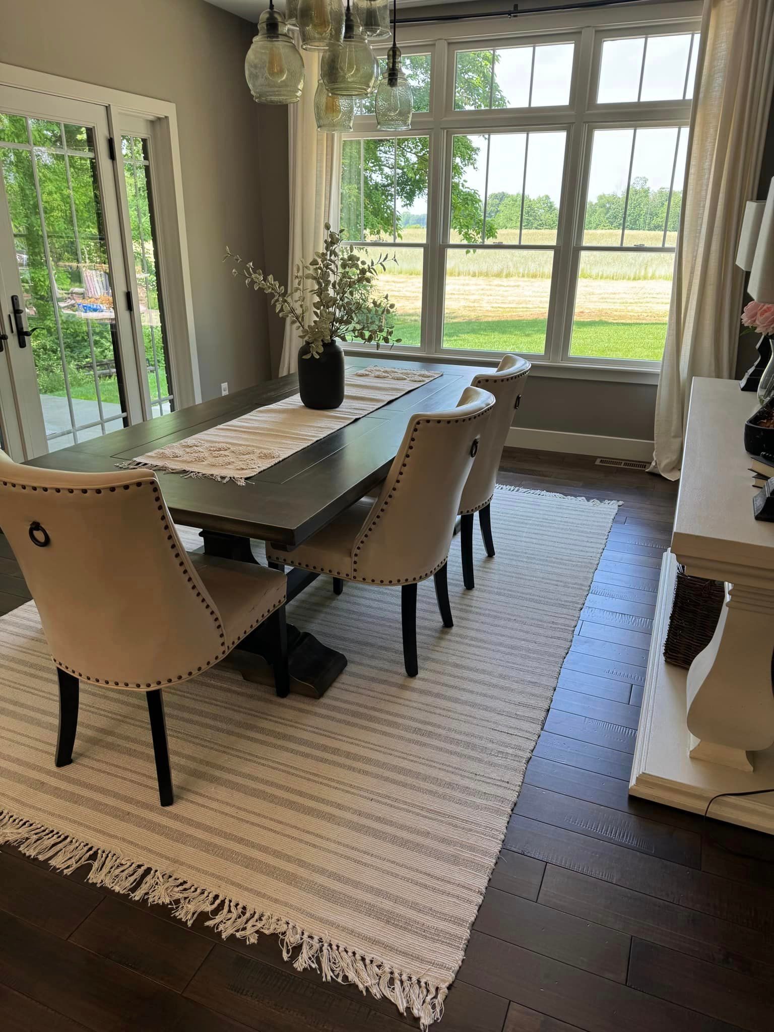 A dining room with a table and chairs and a rug on the floor.