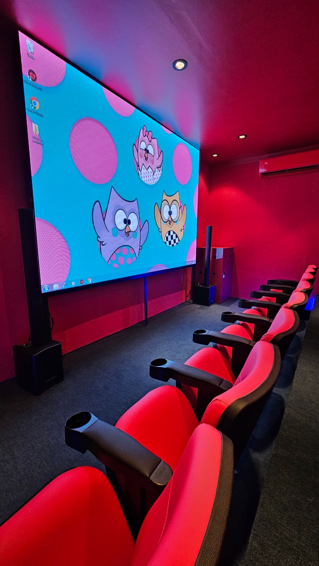 Uma fileira de cadeiras vermelhas em frente a uma tela grande em um cinema.