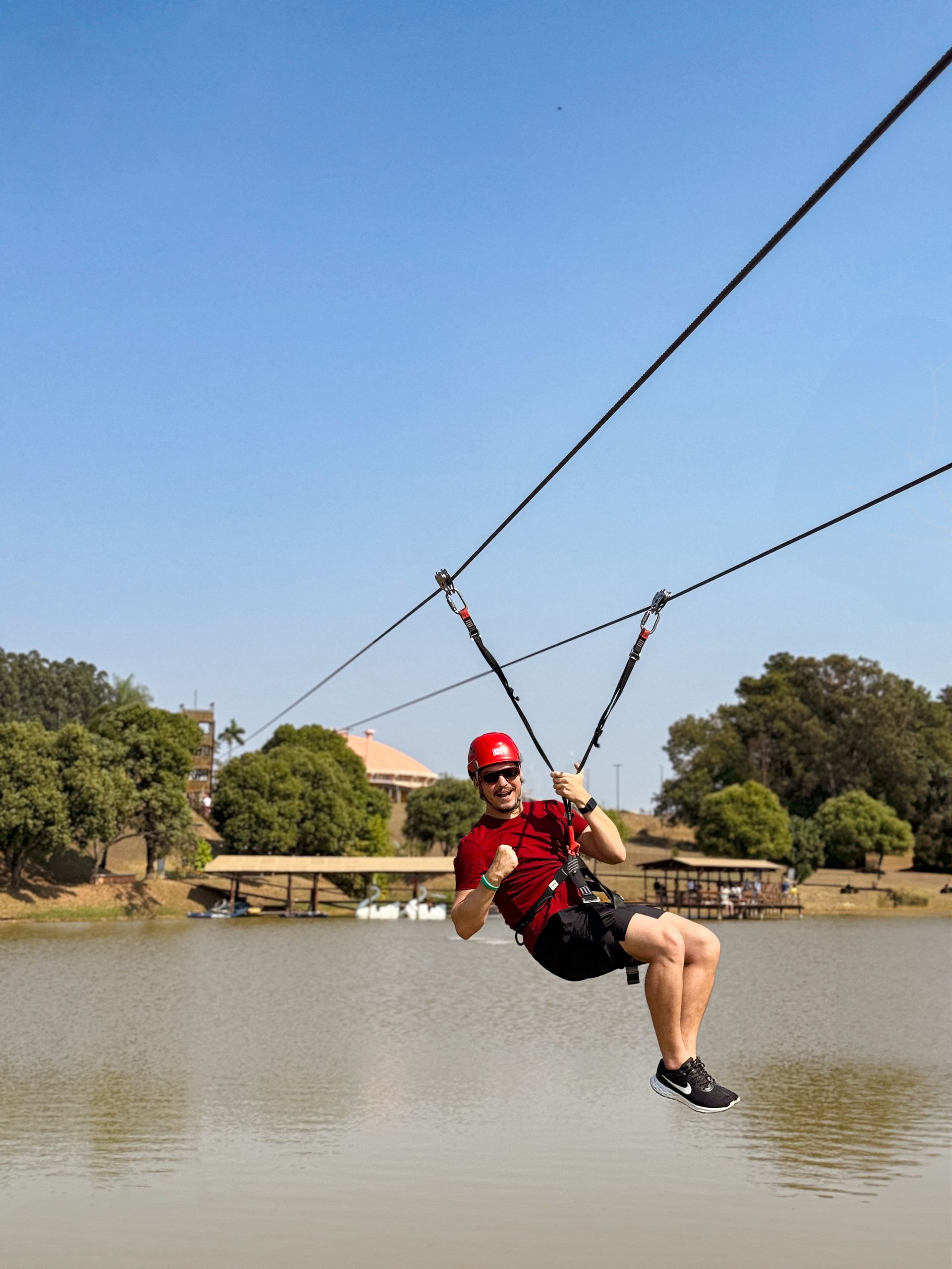 Um homem de camisa vermelha está andando de tirolesa sobre um lago.