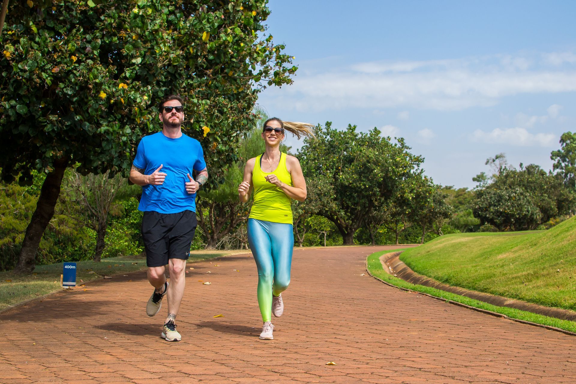 Um homem e uma mulher estão correndo em uma trilha de tijolos em um parque.