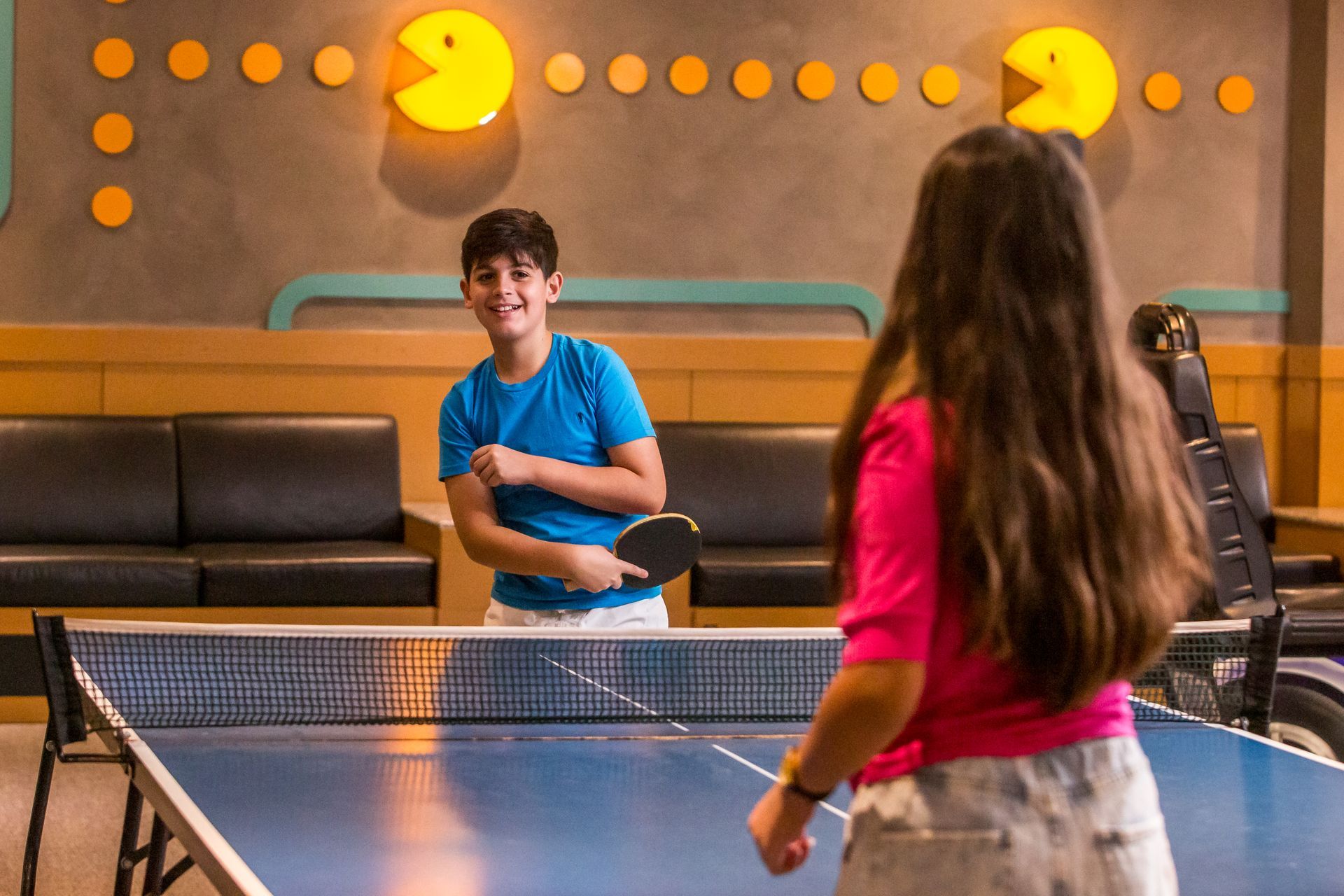 Um menino e uma menina estão jogando pingue-pongue em uma mesa.