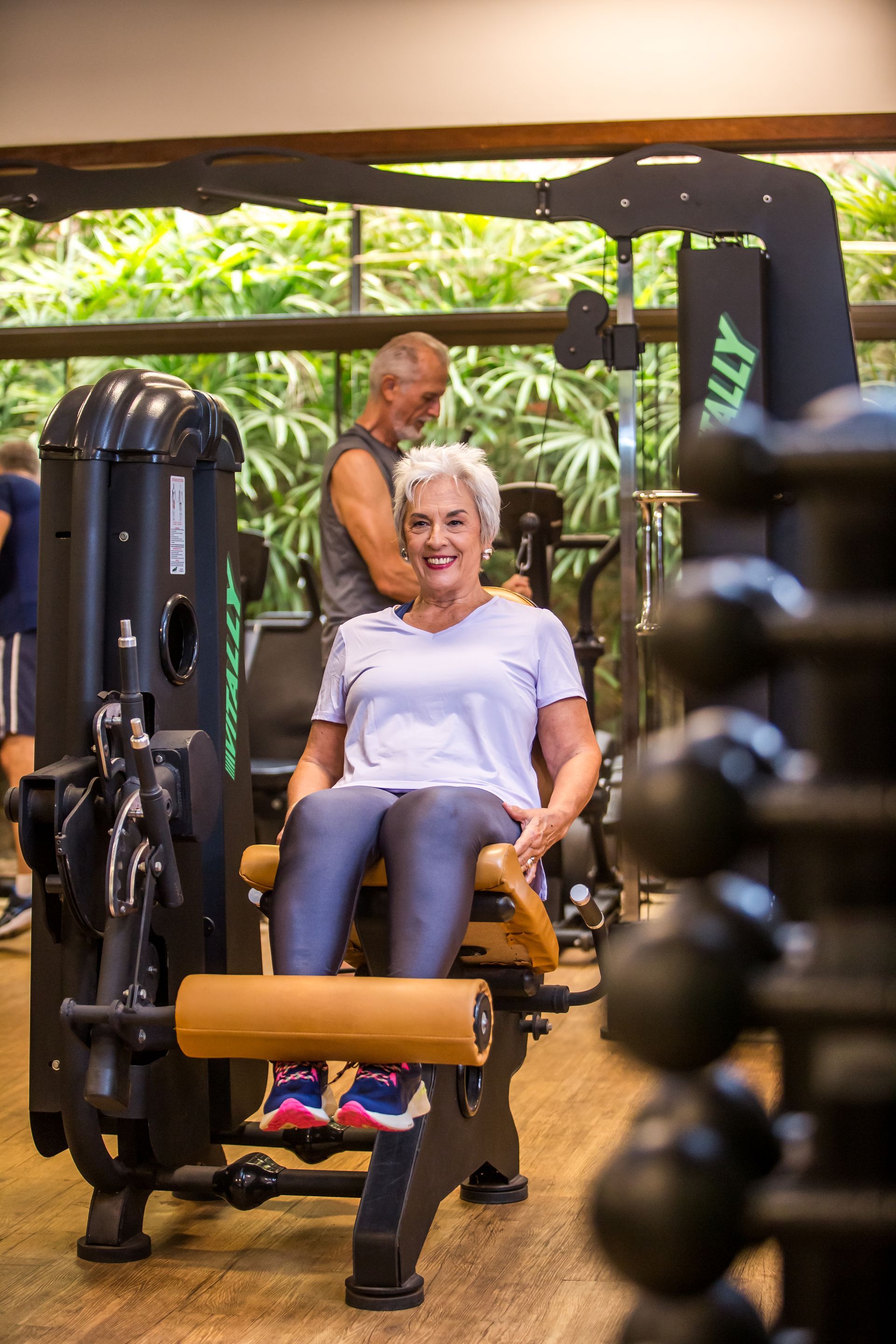 Uma senhora idosa está sentada em uma máquina em uma academia.
